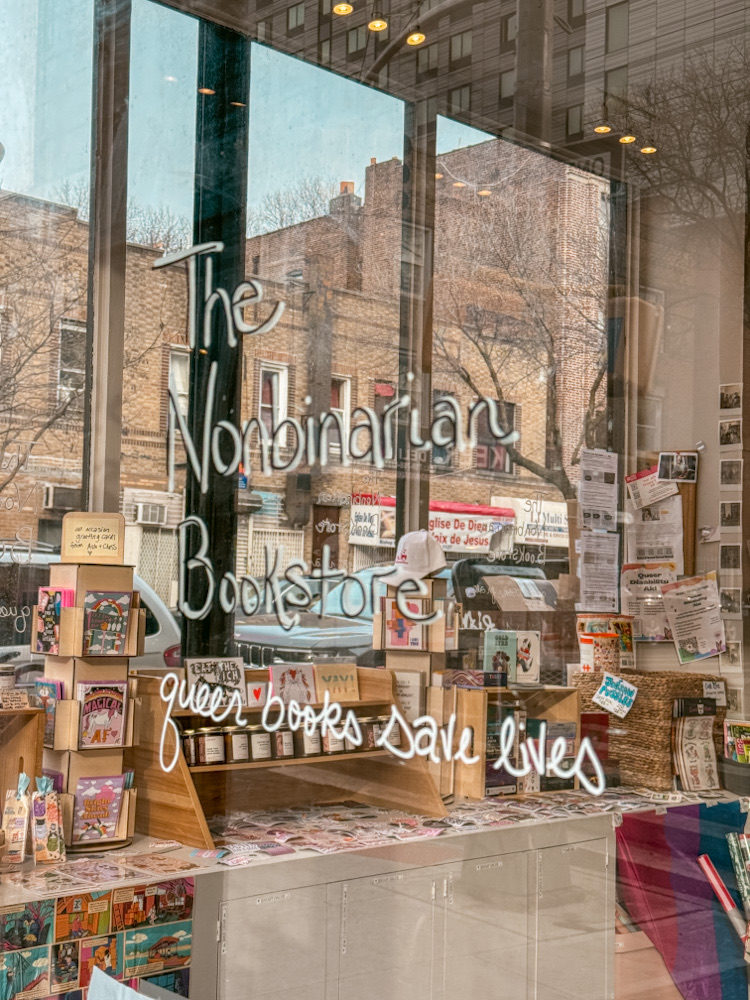 The glass window of a NYC queer bookstore showing its name and the store inside.