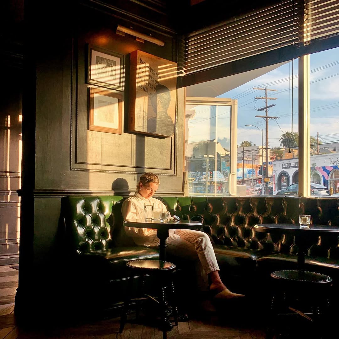 A person in white top and jeans sitting in a bar couch near the windows with sunlight gracing the place.