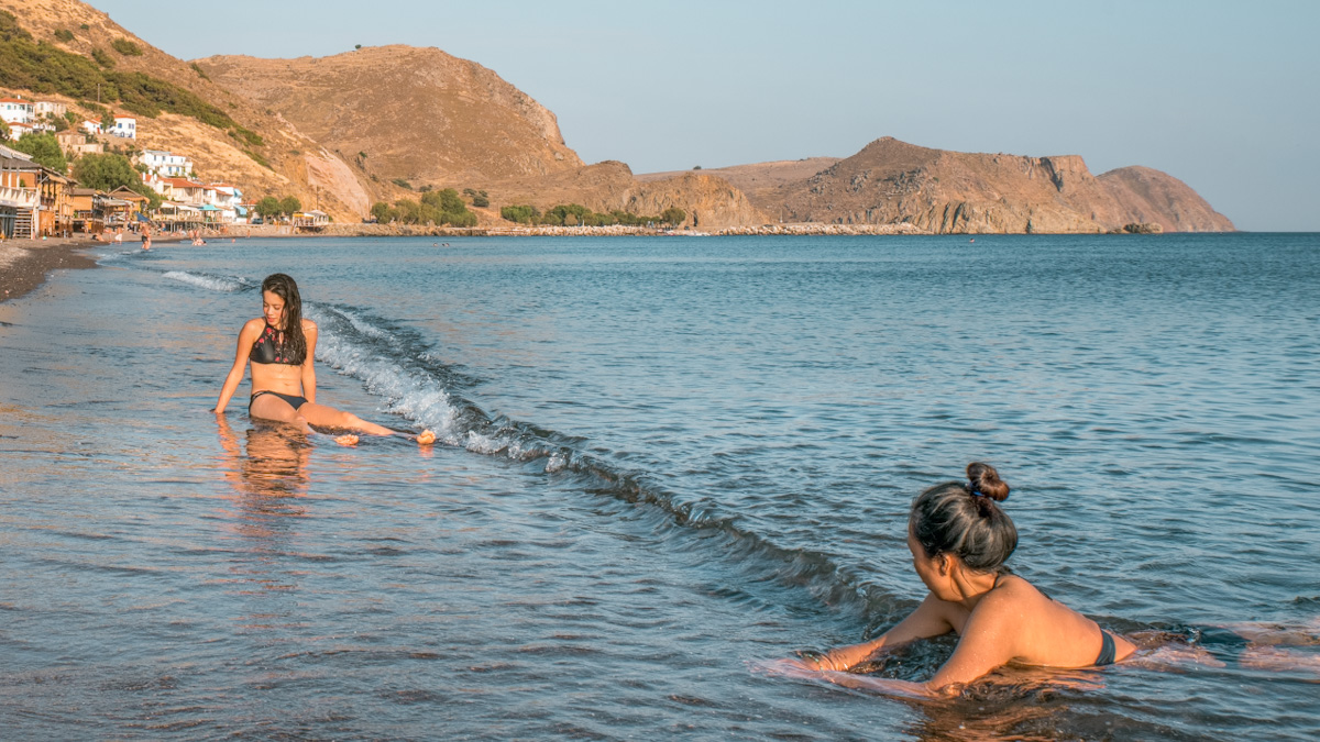 Two women hanging out in the shallow waters of a beach in Greece.