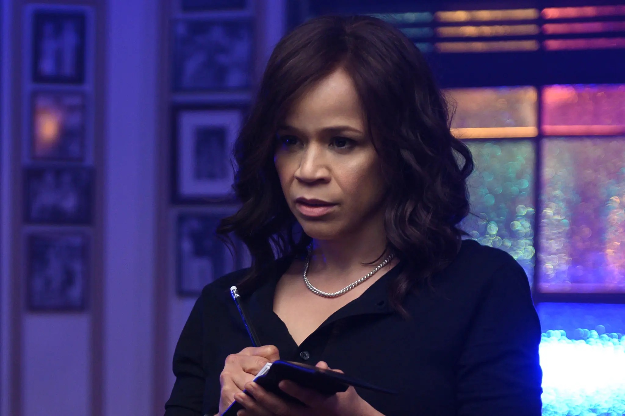 A woman with curly back hair holding a pencil and notepad.